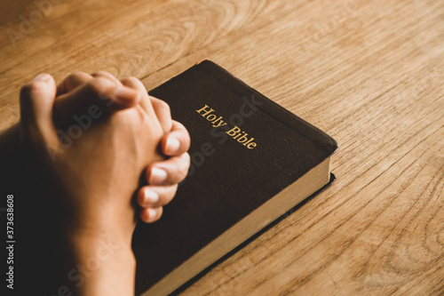 Women praying, Hands clasped together on her Bible in the whiteness over wooden table.