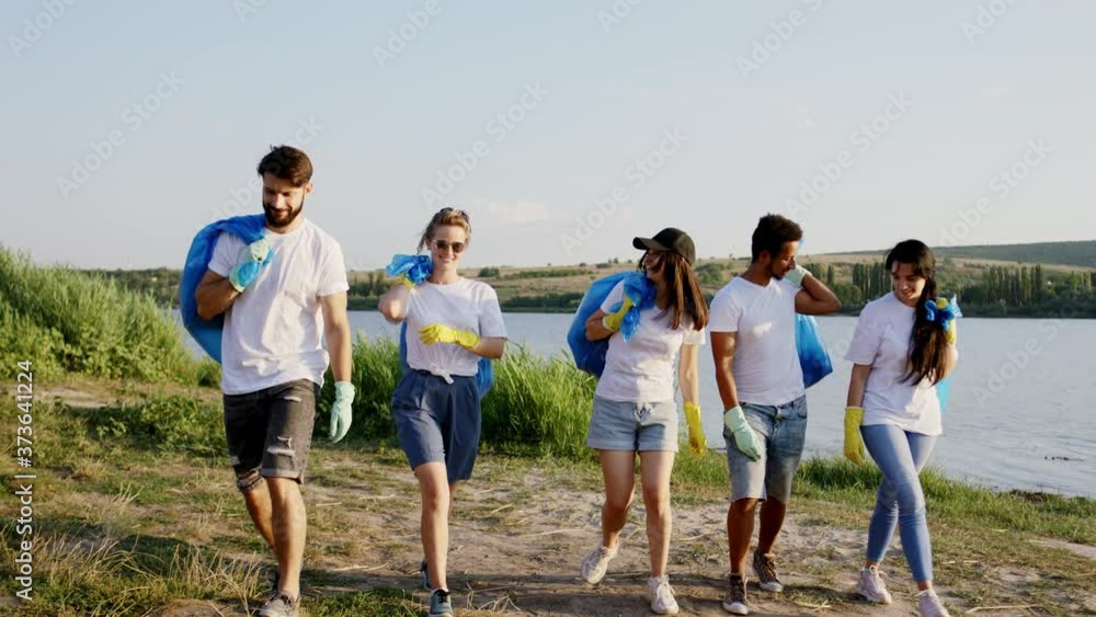 Good looking volunteers on the beach side finish to cleaning up the rubbish and take the big blue plastic bags and start walking in front of the camera happy with a large smile. Shot on ARRI Alexa