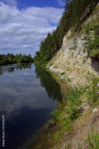 A steep cliff of white gypsum in an outcrop on the right bank of the Iren River in the Kungursky District of the Perm Territory. Hot summer in the foothills of the Western Urals.