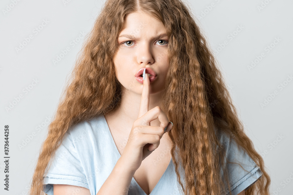 Emotional young woman with curly long hair keeping index finger at her lips, saying Shh, Keep silent, It's secret Emotional young woman with curly long hair keeping index finger at her lips, saying Shh, Keep silent, It's secret