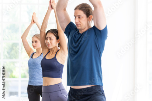  group of diversity Asian and Caucasian young people practicing yoga lesson with instructor. standing in warrior (Virabhadrasana) position. man and woman balancing body. workout healthy and wellness