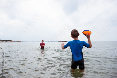 Φωτογραφία Two happy siblings children playing and jumping with ball in water in neoprene s