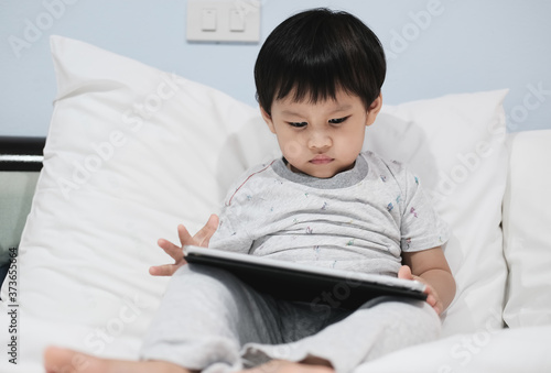 A boy using a tablet computer at home in the bedroom.