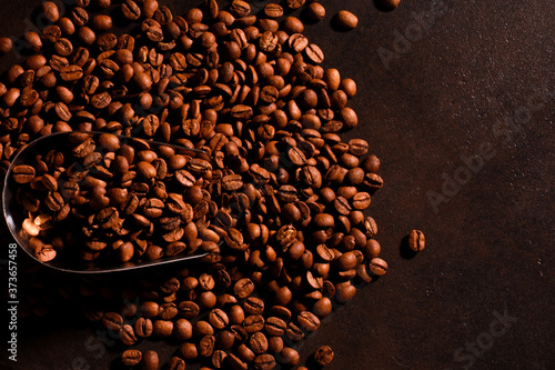 Arabica Coffee beans scattered from metal scoop on dark background. Roasted grains, copy space. Coffee shop, caffeine, roast concept