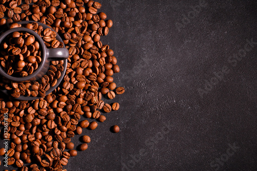 Natural coffee beans in espresso grey cup and on dark background. Roasted Arabica seeds in mug, copy space, top view. Coffee shop, caffeine, roast concept
