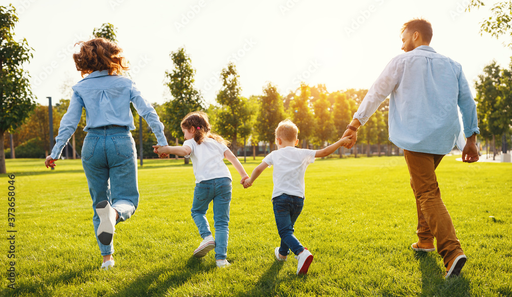 Fototapeta premium Anonymous happy family running back in park in summer evening.