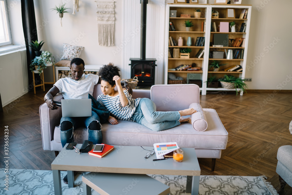 Multiracial couple placing in sofa with credit card and browsing laptop Multiracial couple placing in sofa with credit card and browsing laptop