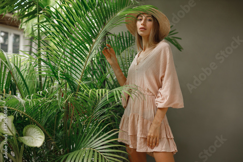 Portrait of happy lady with natural nude makeup, perfect skin, blonde hair. Beautiful woman in straw hat  hiding behind palm leaves. Cosmetic, wellness, purity, skincare, spa concept.