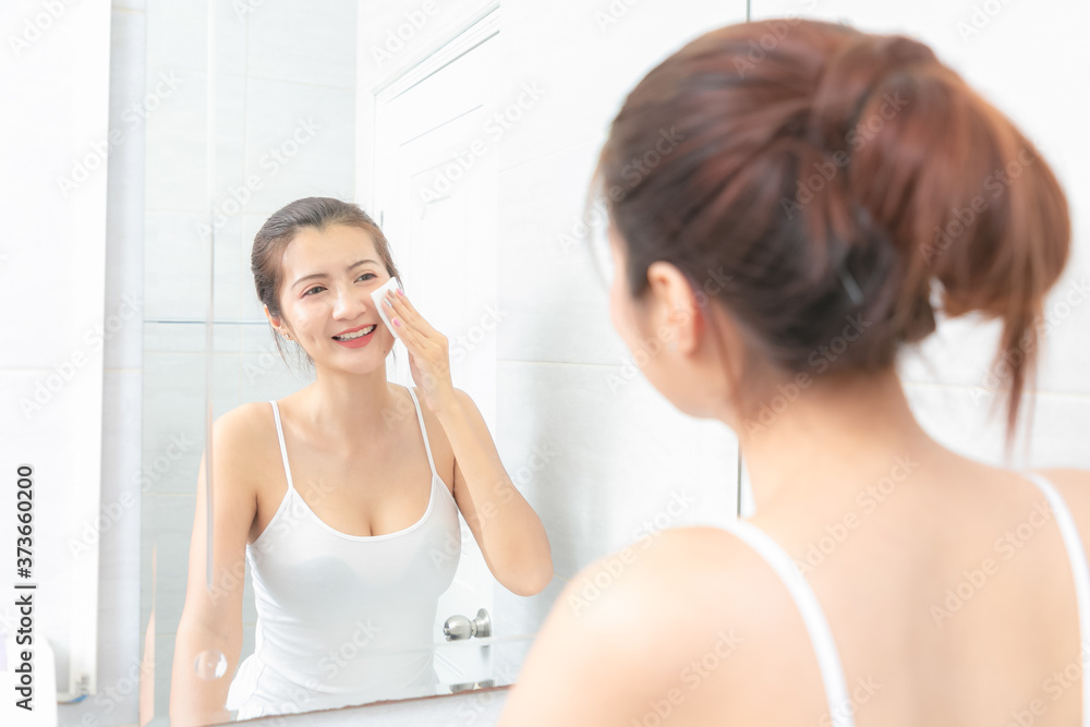 Beautiful Asian Woman applying cosmetic cream in bathroom.