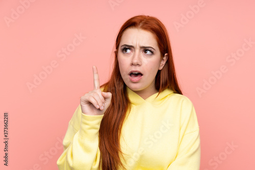 Redhead teenager girl over isolated pink background thinking an idea pointing the finger up