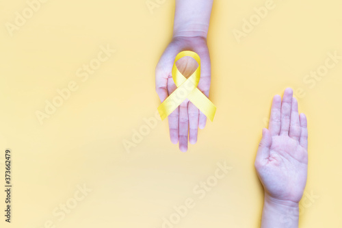 Human hands giving yellow gold ribbon awareness symbol for support suicide prevention, endometriosis, sarcoma bone cancer, bladder cancer, liver cancer and childhood cancer concept. photo