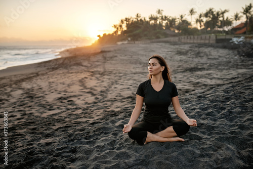 Fototapeta Naklejka Na Ścianę i Meble -  brunette practicing yoga and meditation in lotus position on the background of the sunset and sea.