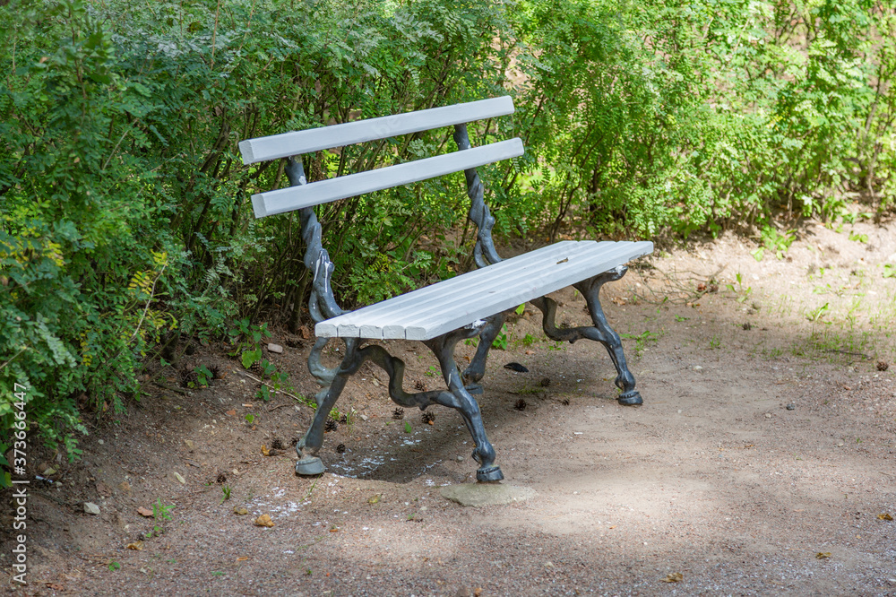 A recreation bench made of white boards and wrought iron in a city park in summer A recreation bench made of white boards and wrought iron in a city park in summer