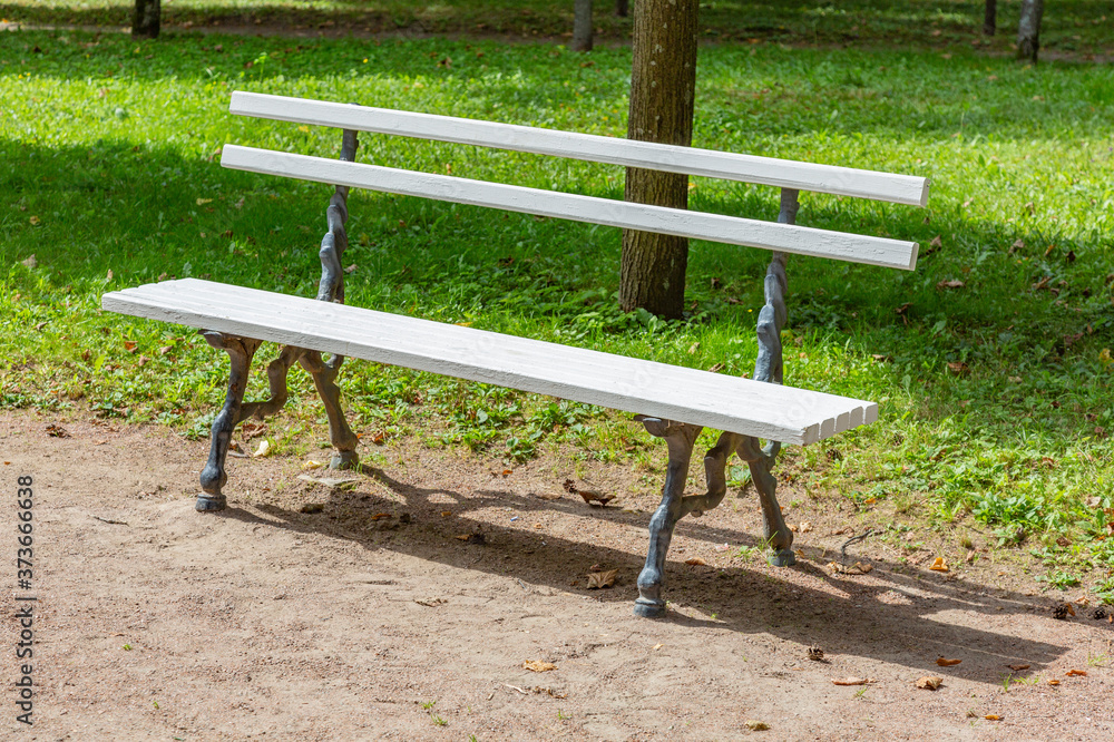 A recreation bench made of white boards and wrought iron in a city park in summer A recreation bench made of white boards and wrought iron in a city park in summer