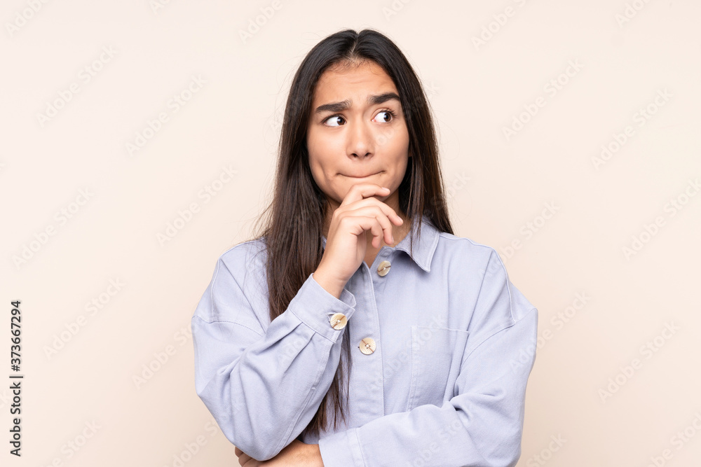 Young Indian woman isolated on beige background having doubts and thinking Young Indian woman isolated on beige background having doubts and thinking