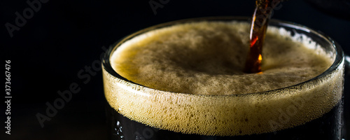 Porter beer pours from a bottle into a mug on a dark background. Panoramic frame, close up and copy space for text