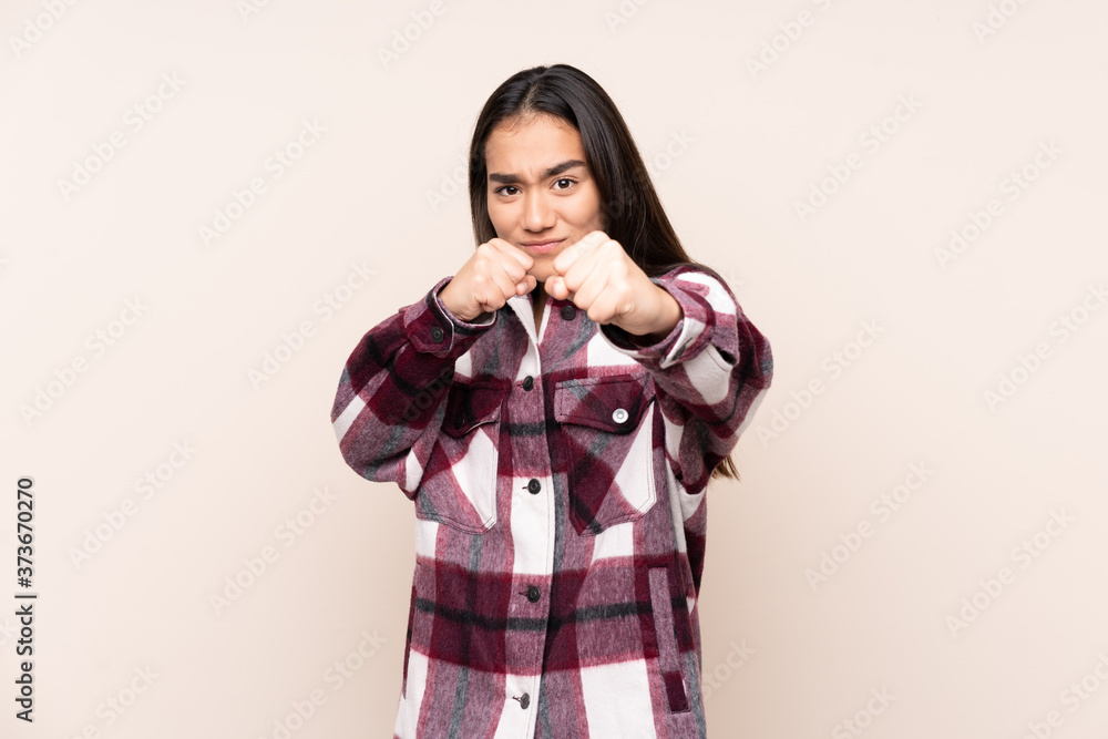 Young Indian woman isolated on beige background with fighting gesture Young Indian woman isolated on beige background with fighting gesture