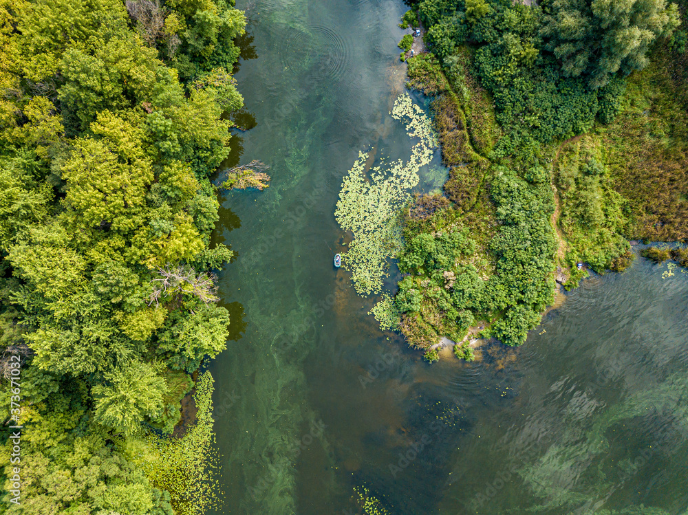 Aerial drone view. Fishing boat on green water near the shore. Algae bloom in the river, green pattern on the water.