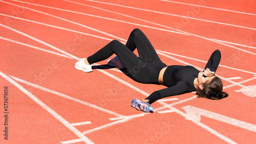 Top view of tired fit woman in sportswear resting after workout or running on a treadmill rubber stadium, holding a bottle of water, taking a break during training, outdoors. 