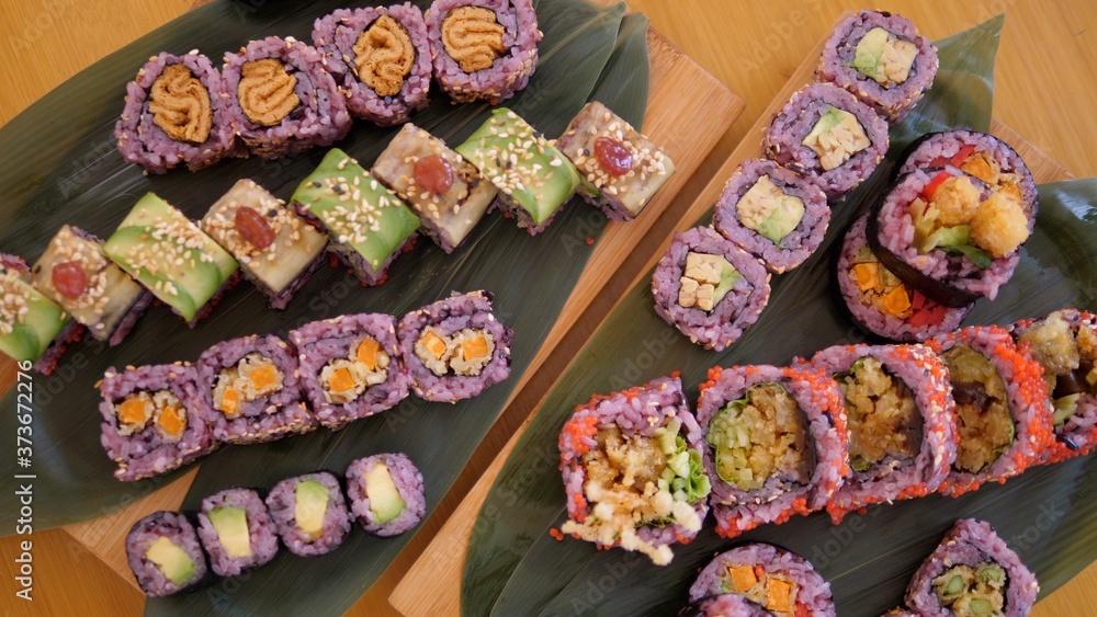 Top view of various sets of colorful vegan sushi rolls with tofu and vegetables. Traditional serving on bamboo leaves and wooden boards.Healthy vegan lifestyle concept