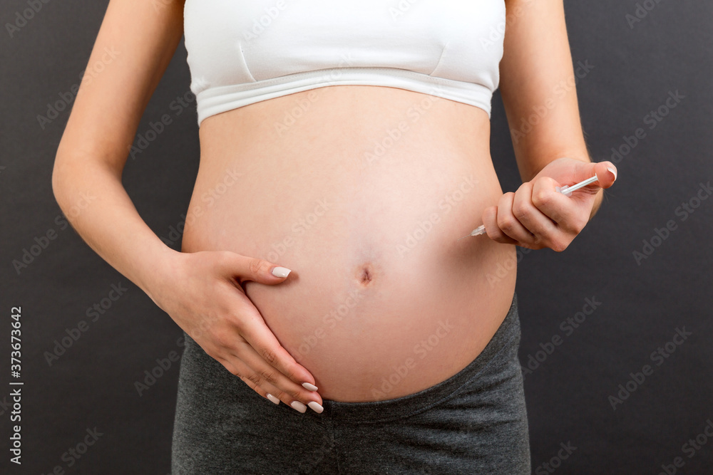 Close up of pregnant woman making injection of insulin in her belly at colorful background with copy space. Sugar control during pregnancy concept Close up of pregnant woman making injection of insulin in her belly at colorful background with copy space. Sugar control during pregnancy concept