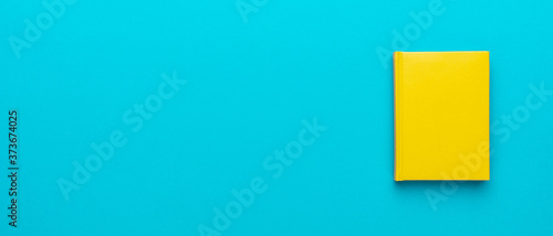 Top view photo of closed yellow notebook over turquoise blue background with copy space. Minimalist flat lay image of closed diary as back to school background.