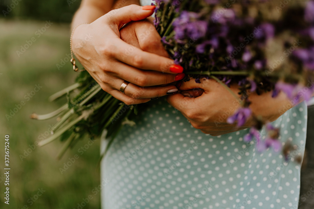 Fototapeta premium holding a bouquet of lilac purple flowers. A woman has a wedding ring on her finger. The girl is dressed in a turquoise dress with peas. Hands of people in love close up.