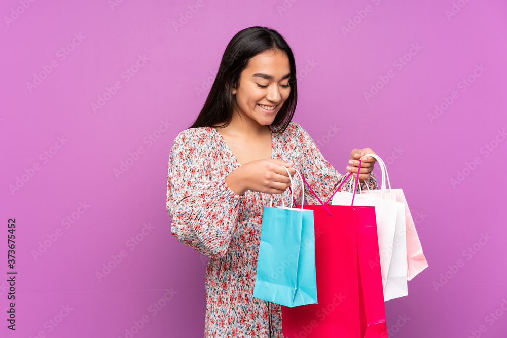 Young Indian woman isolated on purple background holding shopping bags and looking inside it Young Indian woman isolated on purple background holding shopping bags and looking inside it