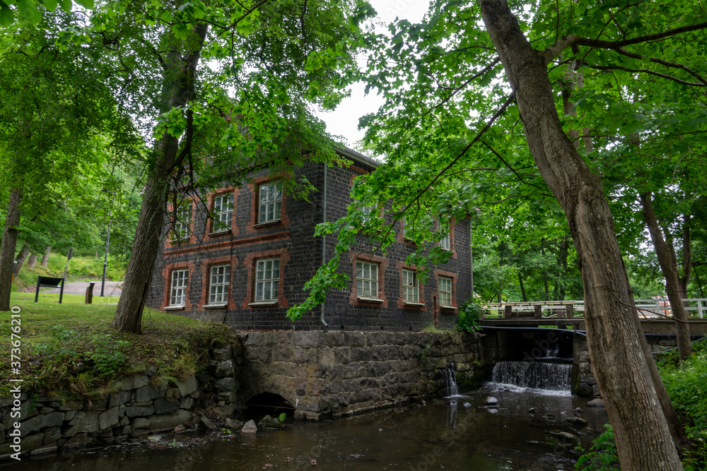 Fiskars village and its mill in the summer time. Former iron works mill built of slag brick (built in 1898). Some trees and a river, Finland.