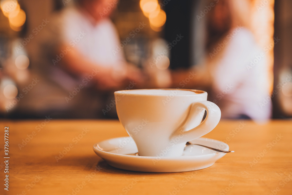 Fototapeta premium Cup with saucer and spoon on a brown wooden table in a cafe