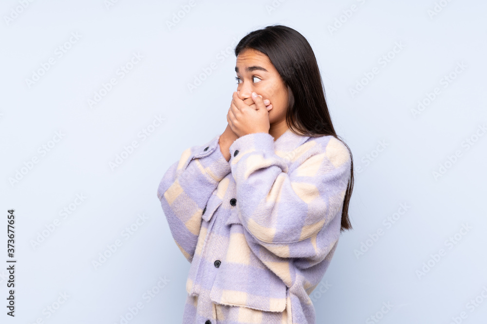 Young Indian woman isolated on blue background covering mouth and looking to the side Young Indian woman isolated on blue background covering mouth and looking to the side