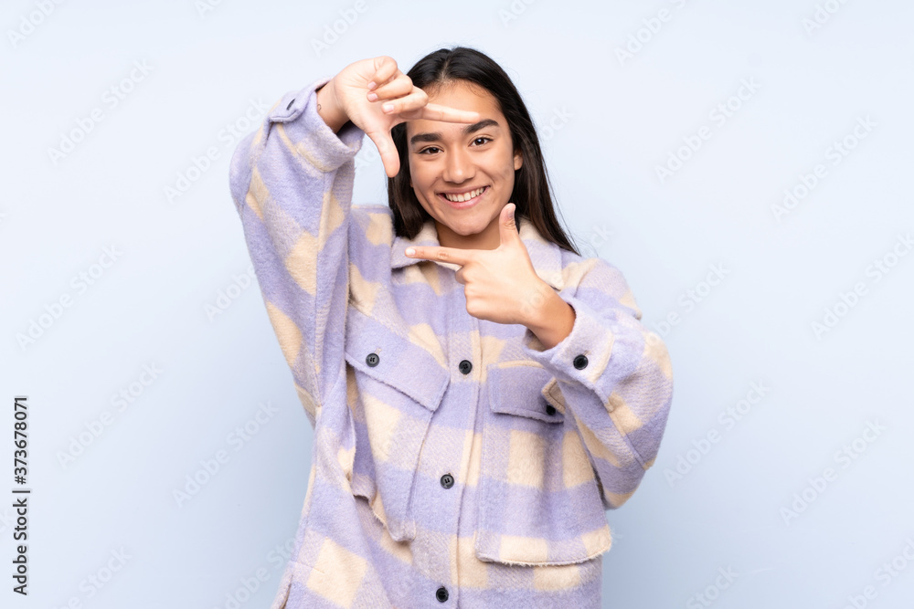 Young Indian woman isolated on blue background focusing face. Framing symbol Young Indian woman isolated on blue background focusing face. Framing symbol