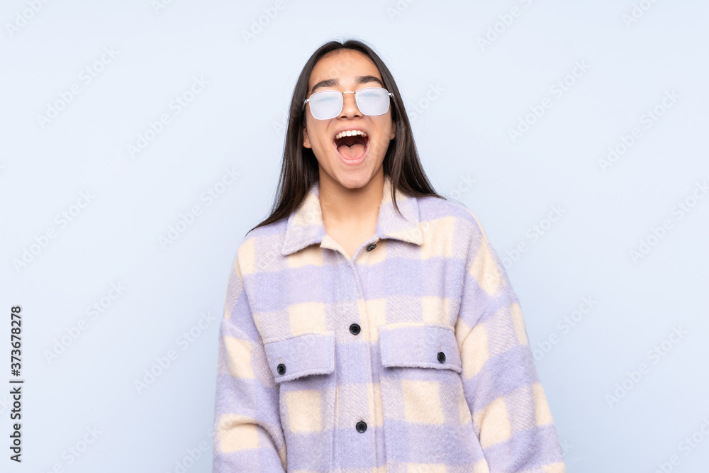 Young Indian woman isolated on blue background shouting to the front with mouth wide open Young Indian woman isolated on blue background shouting to the front with mouth wide open