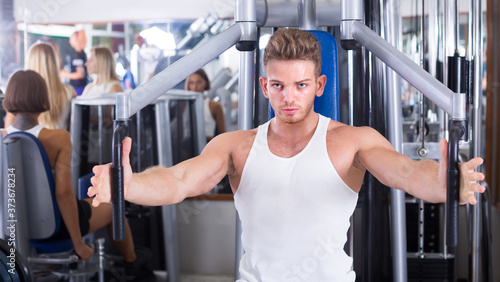 young russian well trained man using pec deck gym machinery indoors