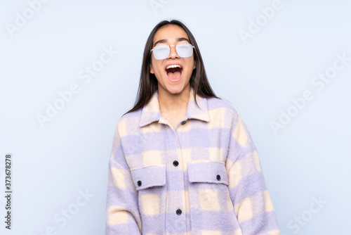 Young Indian woman isolated on blue background shouting to the front with mouth wide open