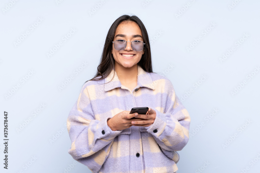Young Indian woman isolated on blue background sending a message with the mobile Young Indian woman isolated on blue background sending a message with the mobile