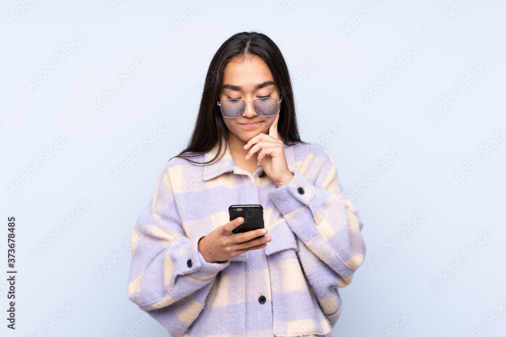 Young Indian woman isolated on blue background thinking and sending a message Young Indian woman isolated on blue background thinking and sending a message