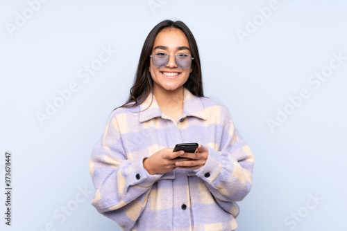 Young Indian woman isolated on blue background sending a message with the mobile