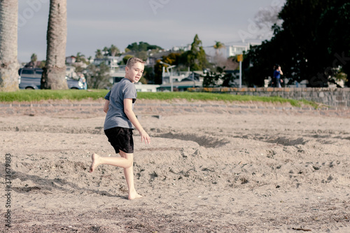 A young boy running on the beach whilst looking backwards over his shoulder.