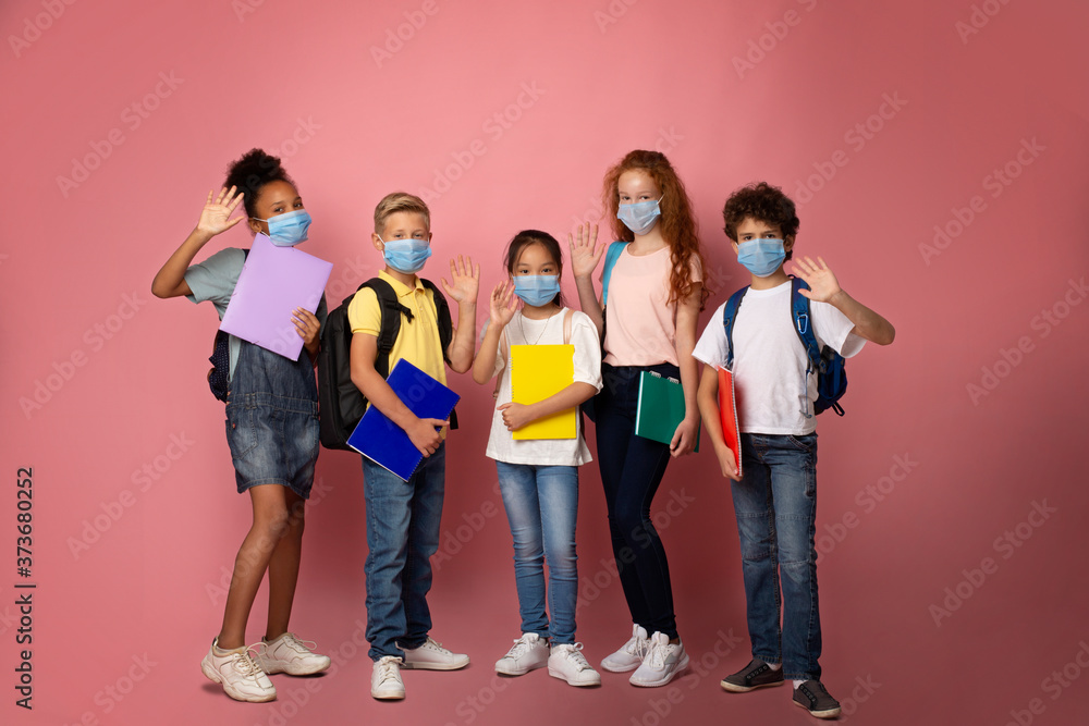 Obraz premium Education during virus pandemic. Full length portrait of schoolkids in medical masks waving on pink background