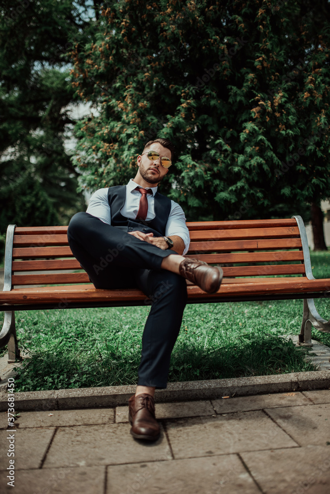 a young sexy businessman in a suit sitting in park on job break a young sexy businessman in a suit sitting in park on job break