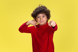 Need you to call. Portrait of pretty young curly boy in red wear on yellow studio background. Childhood, expression, education, fun concept. Preschooler with bright facial expression and sincere