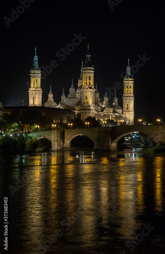 La basílica del pilar de Zaragoza iluminada de noche con el reflejo del puente en el río.