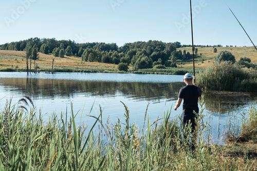 Summer fishing for fishing rod. A fisherman stands against a background of a beautiful, calm lake with reflection of trees. A beautiful scene of outdoor activities