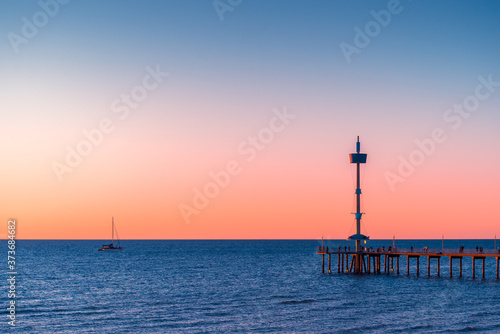Iconic Brighton Jetty with people silhouettes and yacht on the background at sunset, South Australia