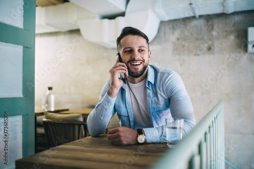 Positive smiling man talking on smartphone in cafe