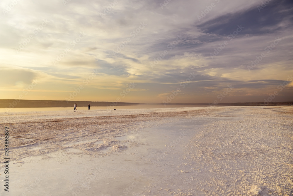 Unique landscape of a salt lake. Salt crystals on the shore and people walking in the water in the distance. Kuyalnik. Ukraine.
