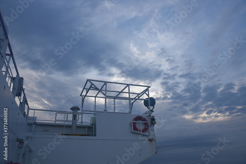 Starboard side wing of navigational bridge of cargo container vessel with the orange life ring, gyro compass repeater, search light and metal frame construction for Panama shelter during overcast sky photo