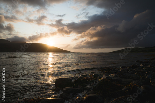 Sunset behind the mountains in font of a bay. Sun setting at the Scottish coast. © Johannes