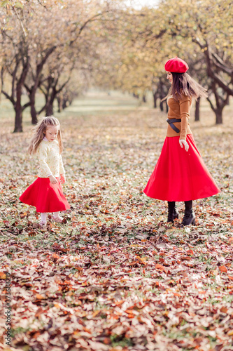 Stylish mom and daughter spend time together in the autumn park. 